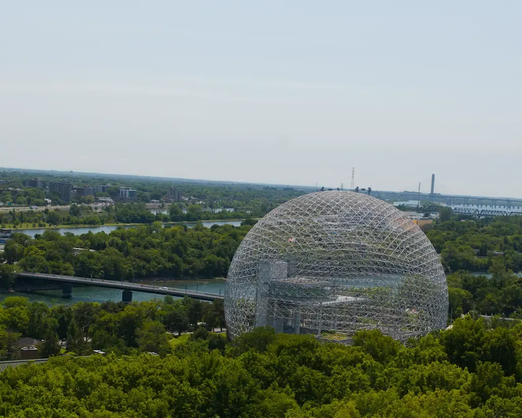 AI generated alt: A large steel geodesic dome among trees, seen from high up, with a river, a bridge and the far bank behind it.